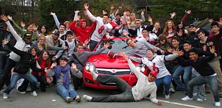 university students surrounding red Saturn Astra